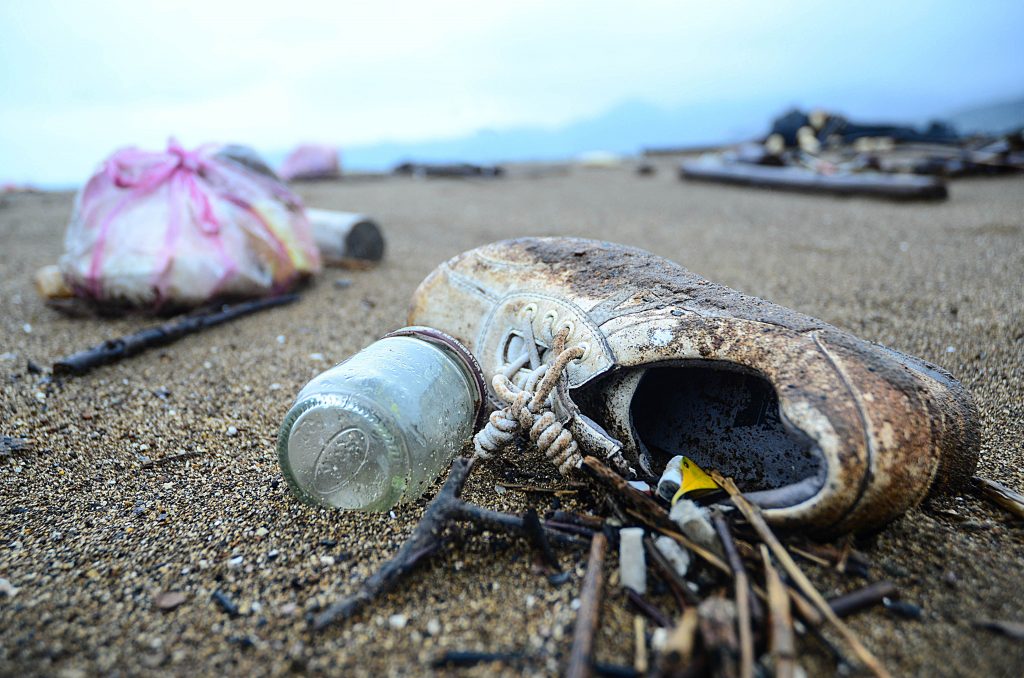 Marine debris scattered on a beach in Taiwan. Photo of a shoe and plastic littering a beach. Photo by Lizane Louw