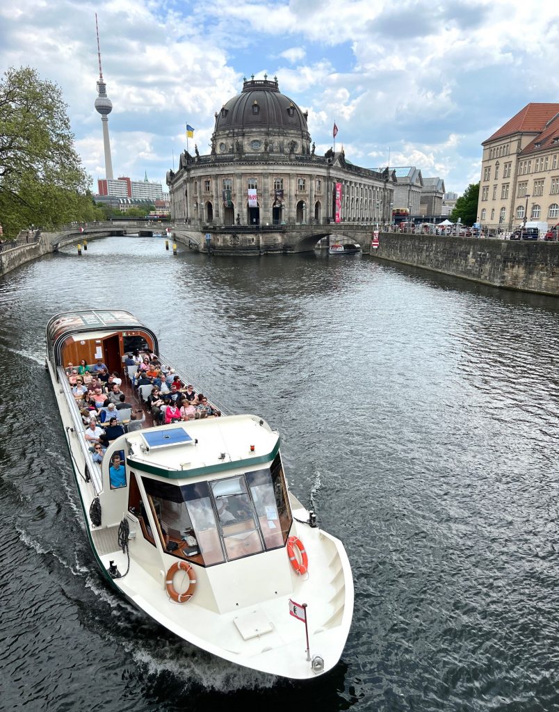 Street photography in Berlin. Photo of a boat on the river Spree. Colourful photo showing architecture in background.